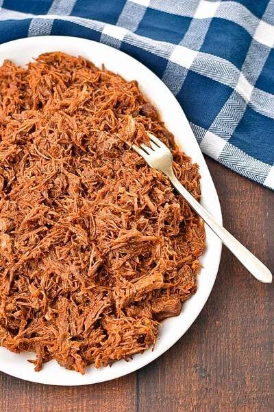 low FODMAP pulled pork on a white platter with a fork in it on a blue and white checkered towel