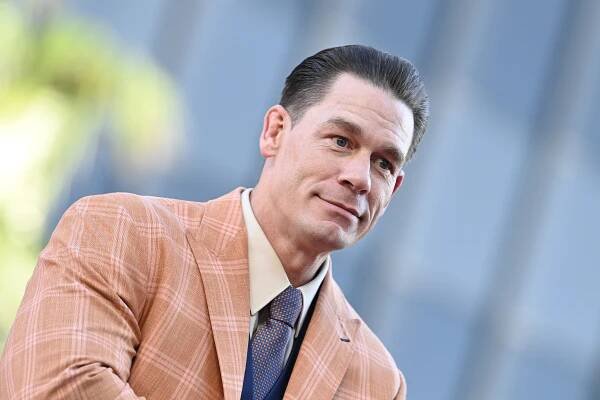 John Cena poses in a peach jacket and purple tie. 