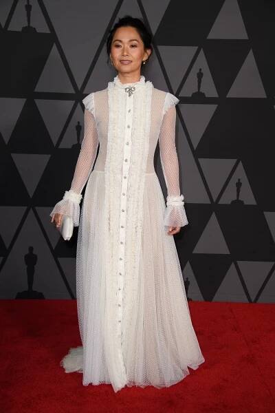 Actress Hong Chau in a white dress on a red carpet against a black backdrop.