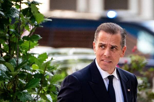 A man in a suit walking near a shrub.