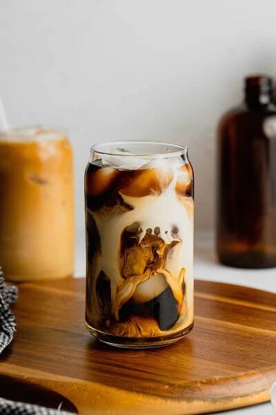 A glass sits on a wooden board filled with cold brew coffee and vanilla sweet cream.