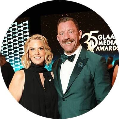 Brent Miller stands in a green tuxedo jacket beside GLAAD President and CEO Kate Ellis, who wears a black evening gown. Behind them, the words 35 GLAAD Media Awards are displayed onstage.
