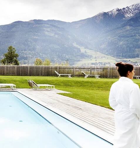 Frau im Bademantel am Pool mit Liegen und Bergpanorama