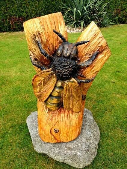 a statue of a bee sitting on top of a wooden stump in the middle of a grass field