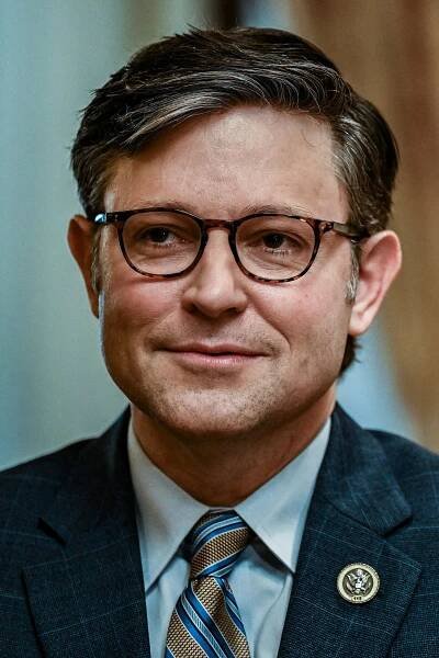 A close-up photo of Speaker Mike Johnson wearing a suit, tie, and glasses.