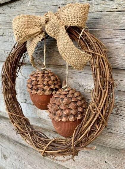 two pine cones are hanging from a wreath on the wall, with a bow around it