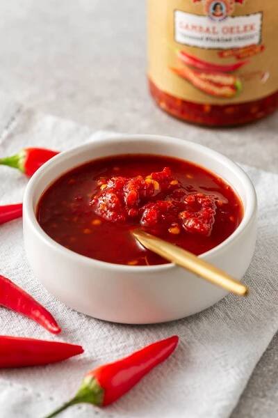 A bowl of bright red sambal oelek next to a jar of shop-bought sambal oelek en fresh chillies.