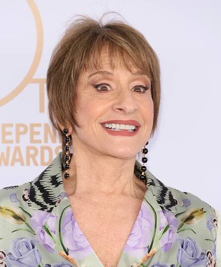 Patti LuPone smiling on red carpet, wearing a floral-patterned blazer with statement earrings