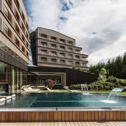 Modernes Hotelgebäude mit Außenpool und Wasserfällen an einem bewölkten Tag.
