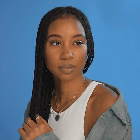 Nia Beckett, a contributing writer for Byrdie poses for a headshot on a blue background. 