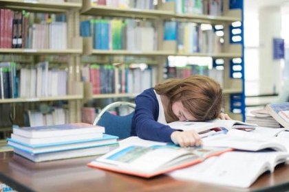 Tired student or young woman with many books sleeping while reading book prepare examination in library at university. People, education, session, exams and school concept
