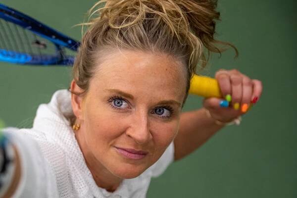 A close-up photo of a woman practicing her tennis serve, keeping her eyes deeply focused on the ball.