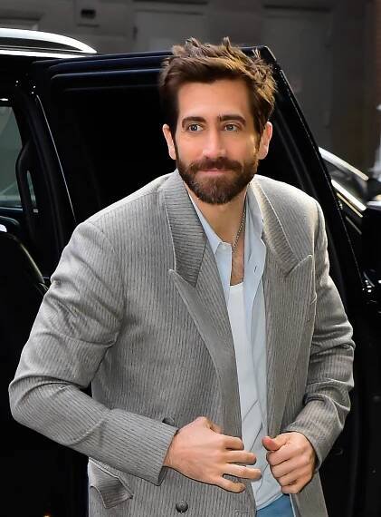 Man with beard wearing a stylish pinstripe suit and white shirt steps out of a car at a celebrity event