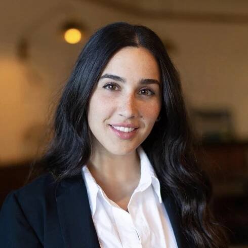 A woman wearing a white button up shirt and black blazer standing and smiling