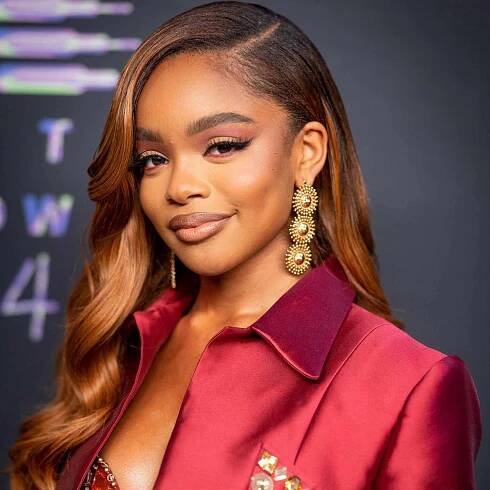Marsai Martin wears a red satin suit, long gold earrings and a deep side part to her copper balayage curled hair