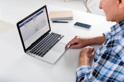 Částečný pohled starší muži, kteří pracují na notebooku s logem Facebooku u stolu s notebookem doma — Stock obrázek