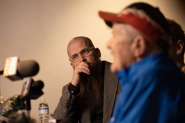Two men sit near a bank of microphones.