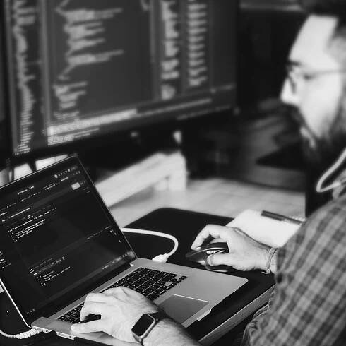 Black and white photograph of a male developer seated at his desk working on computer code.