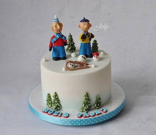 two figurines on top of a frosted cake decorated with snow and trees