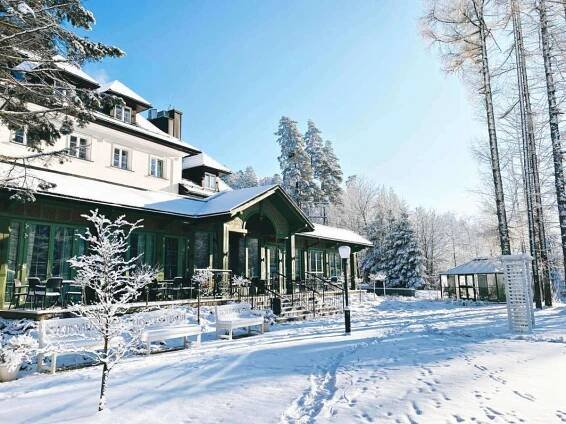 Aries Hotel & Spa Visla Exteriér fotografie The photo shows a beautiful winter scene with a large, multi-story building covered in snow. The building has a light-colored facade with dark green trim around the windows and doors. There's a porch area with outdoor furniture, also dusted with snow
