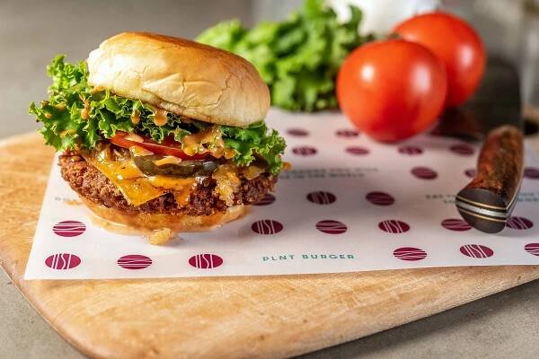 PLNT Burger in bun next to tomatoes