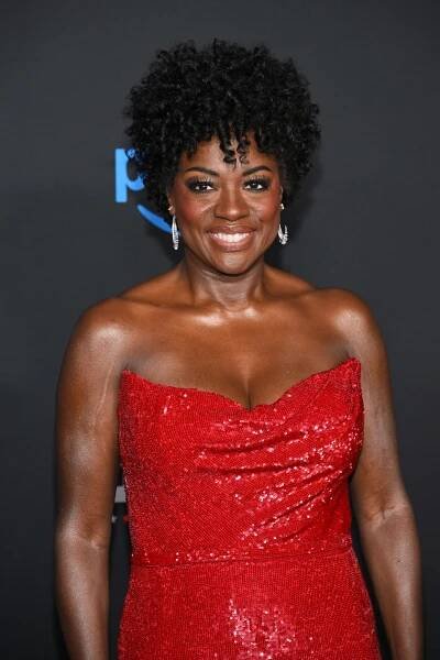 Woman in a strapless, sequined gown posing on a red carpet, smiling