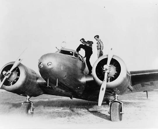 Amelia Earhart and Fred Noonan standing on the wings of an airplane