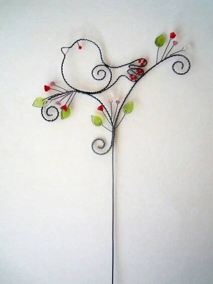 a metal bird on a twig with red berries and green leaves, attached to a white wall