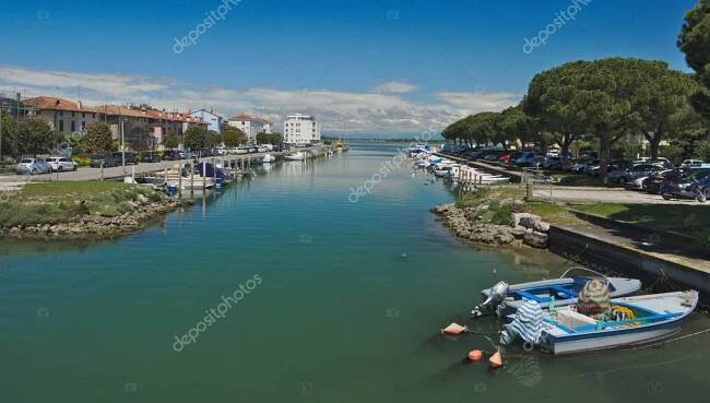 Grado, Grado, Friuli Venezia Giulia Itálie-15. května 2023: Cityscape of Grado, Itálie. Pohled na kanál s motorovými čluny na vodě, moderní budovy a Alpy v pozadí. — Stock obrázek