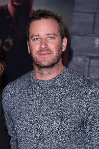 A man in a gray sweater with stubble looks at the camera.