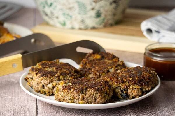Haggis Burgers on a plate with tongs and barbeque sauce in the background
