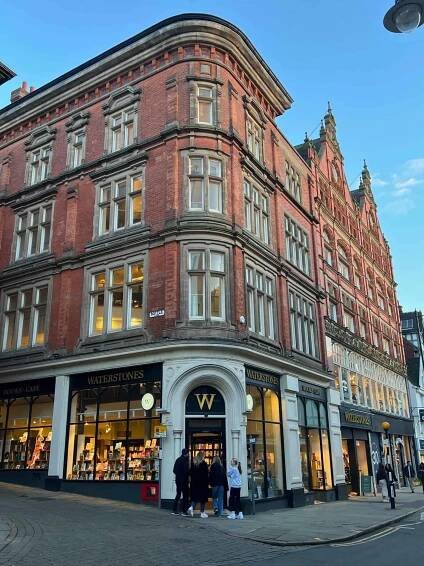 Waterstones Book Shop in a corner red brick building with 4 people walking towards the entrance. 