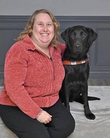 Angela sits with black Lab guide dog Havana for their team portrait