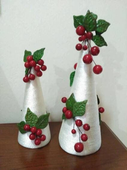 two white vases with red berries and green leaves are sitting on a wooden table