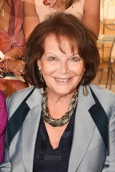 Person smiling at an event, wearing a layered necklace and a striped blazer over a patterned top
