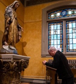 Archbishop Etienne prays the Rosary kneeling before a statue of the Blessed Mother