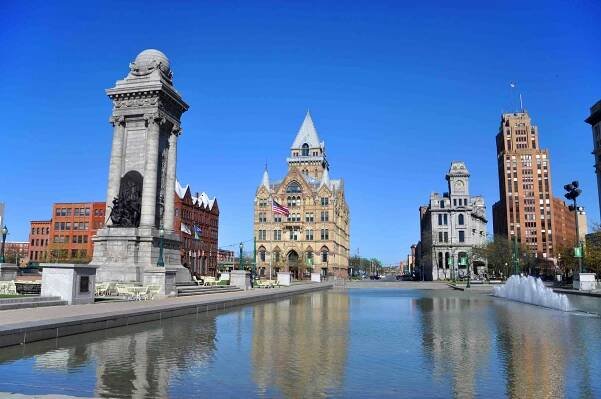 A photo of Syracuse, New York showing a river with a fountain and several large landmarks