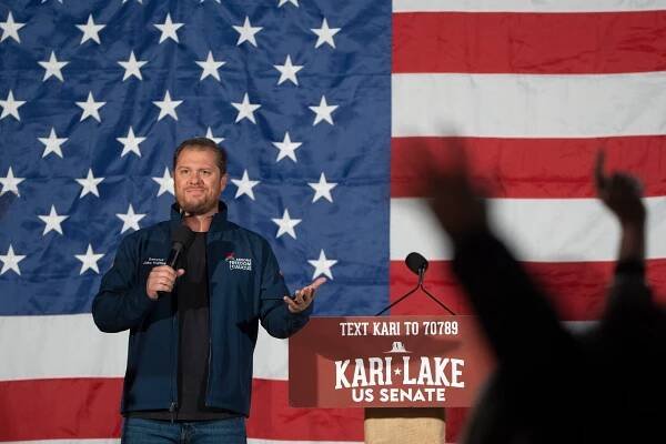 Jake Hoffman speaks into a microphone next to a lectern and in front of an American flag