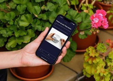 mockuuups-female-hand-holding-an-iphone-13-mockup-in-garden-place