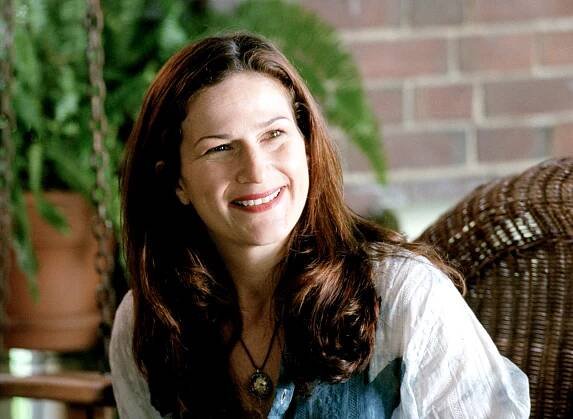 Ana Gasteyer smiling in casual clothing while sitting on a porch chair in "Mean Girls"