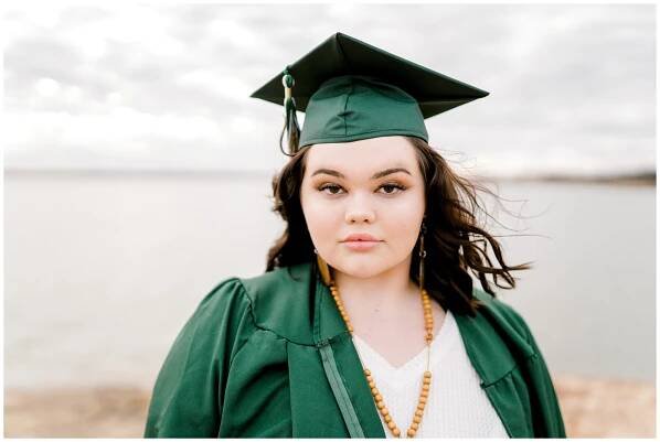 girl standing in cap and gown by lake