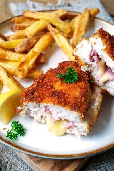 Angeschnittenes Hähnchen-Cordon-Bleu mit Pommes auf einem Teller.