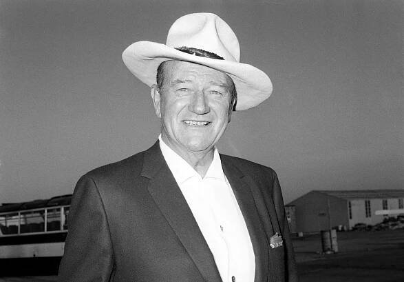 Portrait Photo of the actor John Wayne, wearing cowboy hat and dark suit, facing the camera
