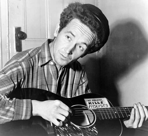 Woody Guthrie pose pour un portrait avec sa guitare sur laquelle est inscrit « Cette machine tue les fascistes »  (1943)