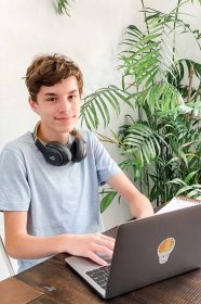 teen boy sitting at table doing homework on a laptop