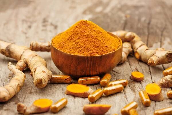 Turmeric powder in wooden bowls and turmeric capsules on a wooden background, highlighting the health benefits of curcumin
