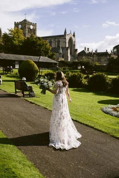 A bride gracefully making her way down a path towards the magnificent Hexham House, creating an enchanting wedding scene.