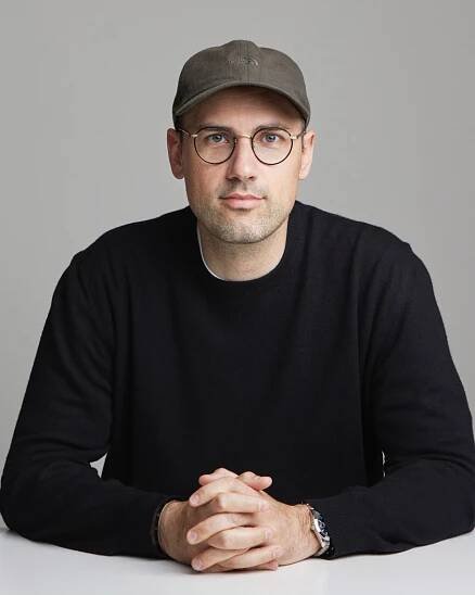 Portrait of David Fischer sitting at a table wearing a black jumper and cap