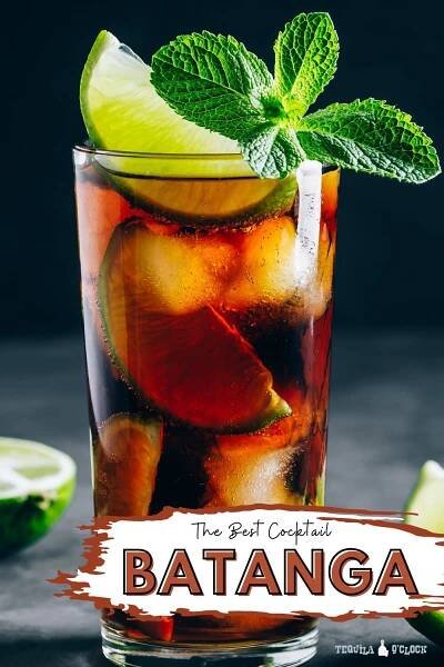 A glass of coke with tequila, lime slices and a mint sprig topping