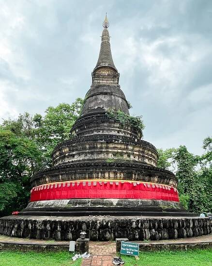 Mossy circular chedi wrapped in red cloth at Wat Umong, nestled in a quiet wooded area. 
